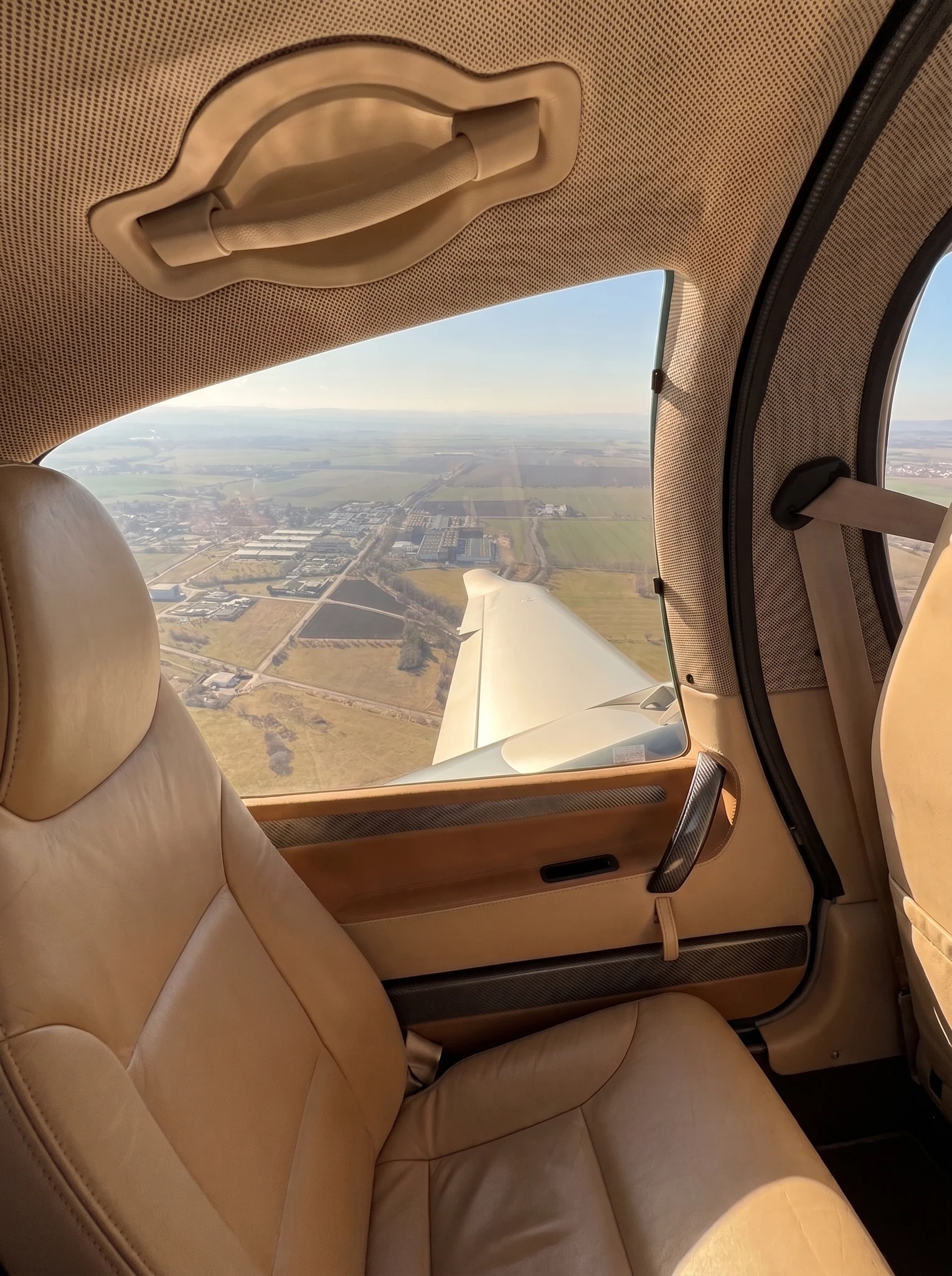 An empty beige leather window seat with a view over the wing